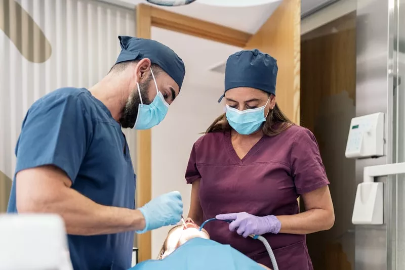 dentista a obturar o dente de um paciente num consultorio, com a ajuda da assistente 